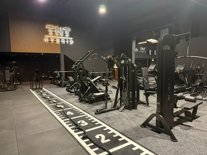 TNT Hybrid illuminated signage above the strength floor with sled track, plate-loaded machines and benches
