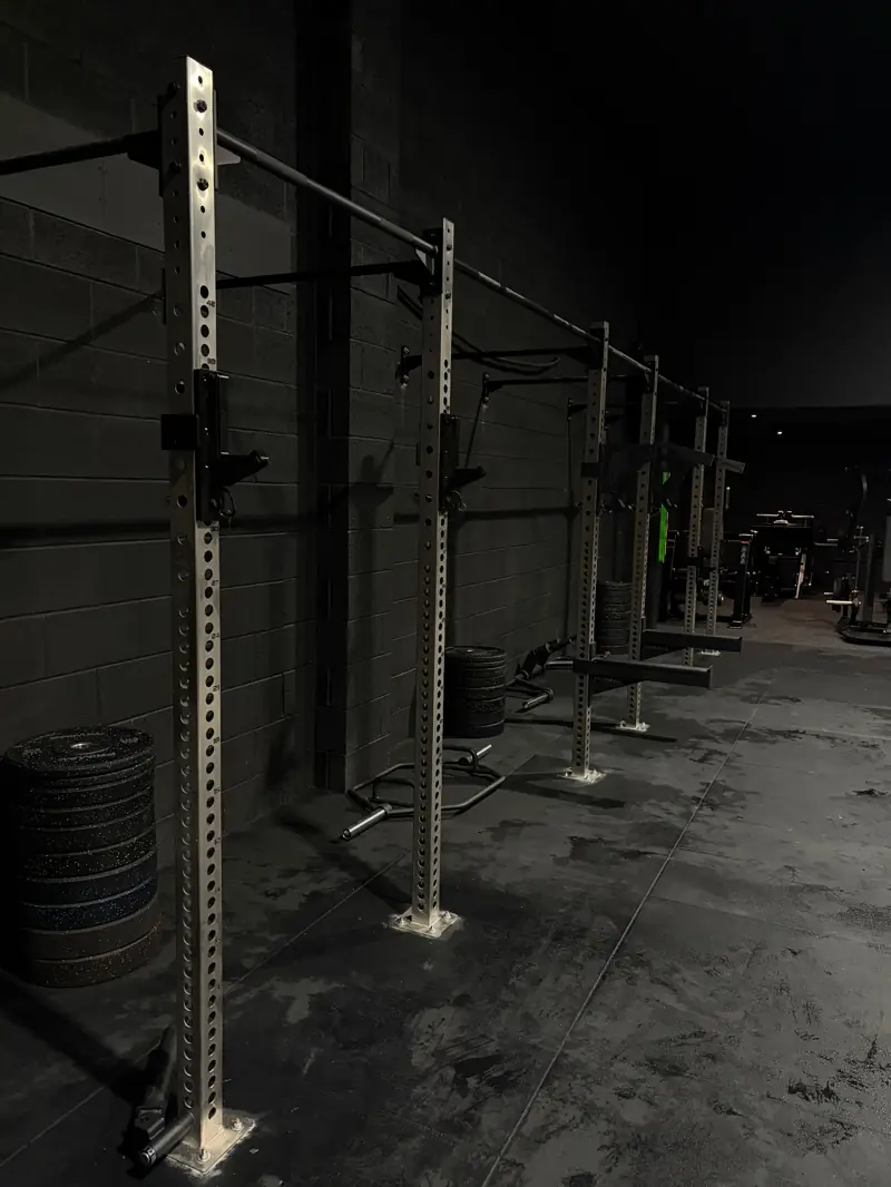 Heavy-duty squat racks lined against the wall with stacked bumper plates on the strength floor